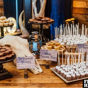 Rustic dessert table display with brownie bites, cake pops, and mini cream pies on wooden surface.