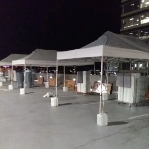White pop-up event tents with weighted bases set up on concrete at night.