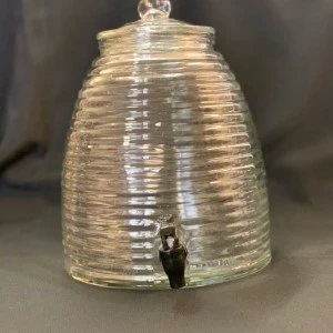 Glass beehive-shaped beverage dispenser with textured ribbed design and metal spigot for event catering.