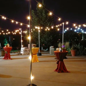 Outdoor nighttime event space with string lights, white poles, red table linens, and an empty dance floor.