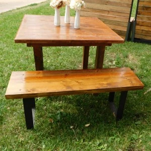 Rustic wooden picnic table with matching bench on green grass outdoor setting.