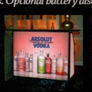 Absolut Vodka display with multiple colorful glass bottles on branded advertising board.