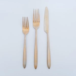 Three sleek gold-toned forks and knives with minimalist design on white background.