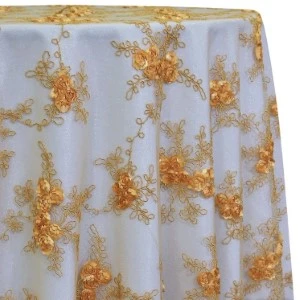 Sheer gold floral lace overlay fabric with delicate embroidered design on light background.