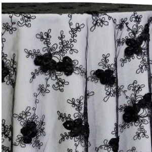 White and black floral lace fabric with textured black rosette clusters on draped curtain.