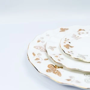 Delicate white ceramic plates with gold floral pattern stacked elegantly on soft background.