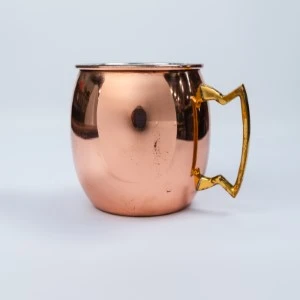 Copper Moscow mule mug with gold decorative handle on white background.