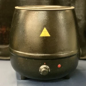 Bronze electric food warmer with yellow triangle emblem and round temperature control knob.