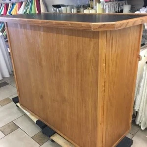 Wooden curved bar with rounded edges and warm wood grain, positioned on tile flooring in event space.