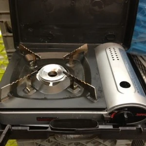 Portable stainless steel camping stove with four-pronged burner and silver casing.