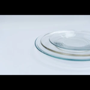 Stacked clear glass dinner plates with smooth, translucent edges on white background.