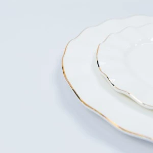 Delicate white ceramic plate with subtle gold rim, stacked on minimalist surface.