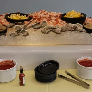 Seafood buffet display with oysters, shrimp, and condiments on ice-filled serving tray.