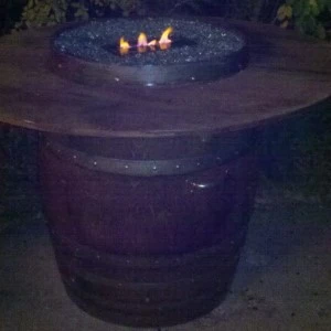 Dark barrel-style fire pit table with three flames burning against a dim evening backdrop.