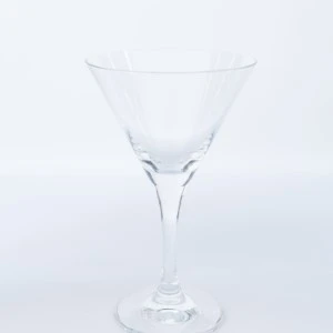Clear glass martini cocktail coupe with wide rim and slender stem on white background.