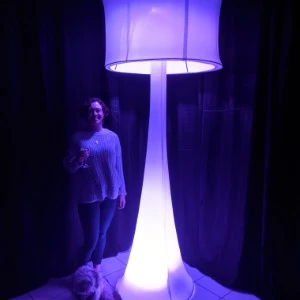 Large illuminated purple floor lamp with curved base and glowing person standing nearby.
