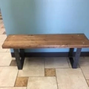 Rustic wooden bench with dark metal legs on tile flooring against blue wall.