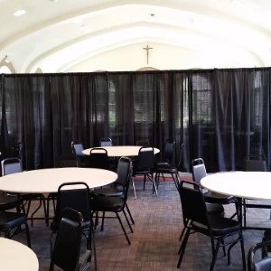 Round white event tables with black chairs arranged in draped room with arched ceiling.