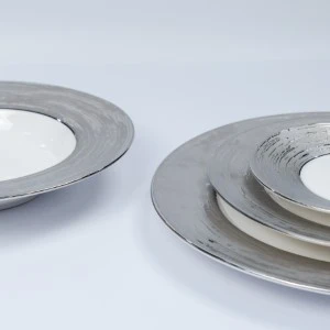 Stacked gray ceramic dinner plates with wide metallic rim and subtle textural details.