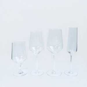 Four clear glass champagne flutes with long stems arranged on a white background.