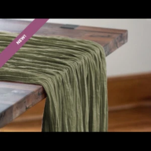 Olive green draped fabric with soft, flowing texture cascading over wooden table edge.