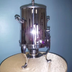 Stainless steel coffee urn with reflective surface on wooden round event table.