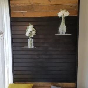 Dark wooden wall display with two white floral vases on floating shelves.