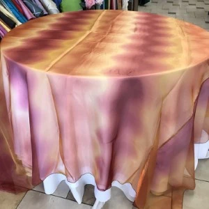Sunset ombre tablecloth in shimmering orange, pink, and gold tones with soft fabric draping.