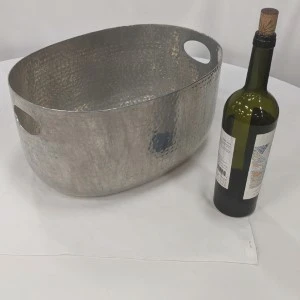 Silver metallic oval bucket with handles next to green wine bottle on white surface.