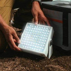 White LED lighting panel with grid pattern held by hands, positioned on dark textured surface.