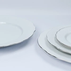 Stacked white porcelain dinner plates with thin silver rim, minimalist event tableware set.