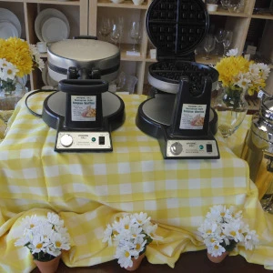 Yellow gingham linen with two professional waffle makers and white floral decor on display.