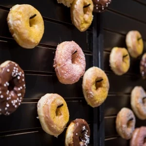 Assorted glazed donuts hanging on dark metal rack with chocolate and pink varieties.