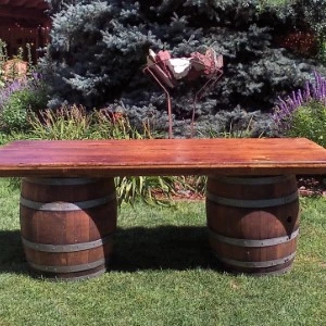 Rustic wooden bench with wine barrel bases on green grass, flanked by lavender and evergreen shrubs.
