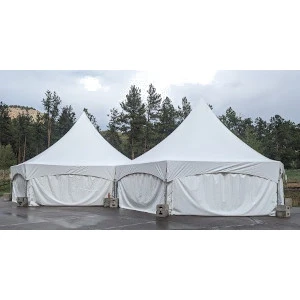 Two white high-peak frame tents with curved side walls sit on pavement, surrounded by pine trees in background.