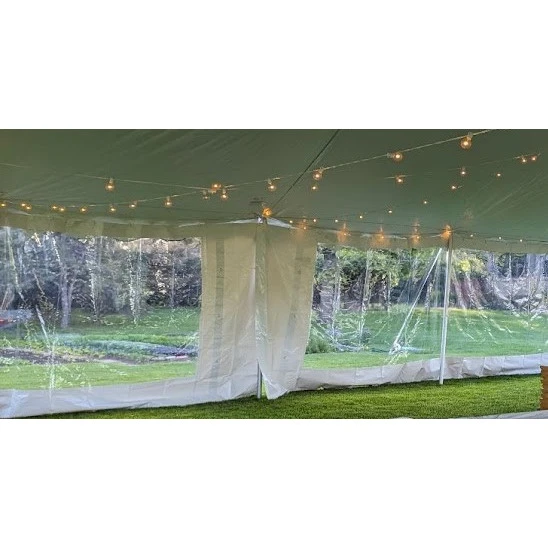 White-trimmed clear frame tent with string lights, green grass, and transparent sidewalls set in wooded garden.