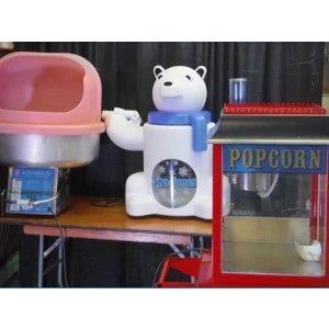 Blue-white bear-shaped popcorn machine sits next to pink chair and red popcorn maker on rental display shelf.