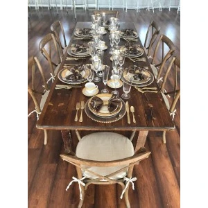 Rustic wooden dining table set with bronze chargers, gold-rimmed glassware, and elegant cross-back chairs on.
