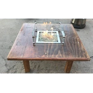 Rustic wooden coffee table with glass fire pit insert on gray concrete surface.