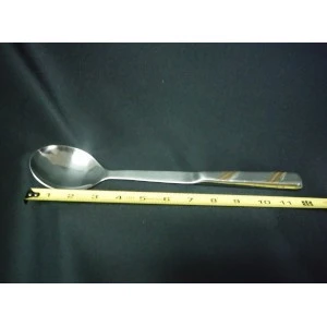 Stainless steel serving spoon with long handle rests on yellow measuring tape against dark background.