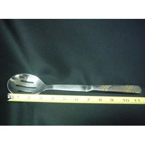 Stainless steel slotted serving spoon with long handle measured against yellow ruler on dark background.