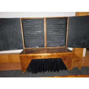 Wooden event table with black skirt, framed by dark chalkboards and warm wood paneling in rustic interior.