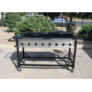 Stainless steel commercial griddle with multiple burners mounted on black wheeled cart outdoors.