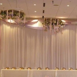 White draped event space with soft gold chairs, hanging floral chandeliers, and sheer elegant ceiling decor.