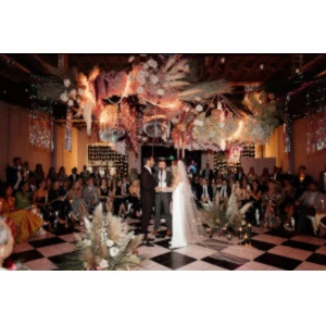 Dramatic wedding reception with black and white checkerboard dance floor, white-clad couple, and ornate ceiling.