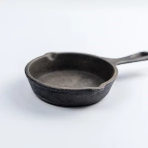 Cast iron skillet with rustic dark patina, smooth surface, and long handle against white background.