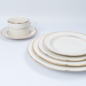 Ivory ceramic dinnerware set with delicate gold rim, featuring stacked plates and matching teacup.