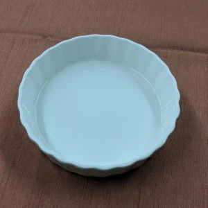 Pale blue ceramic baking dish with scalloped edges and smooth glazed interior on brown surface.
