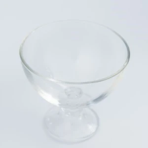 Transparent glass dessert dish with slender stem and curved bowl on white background.