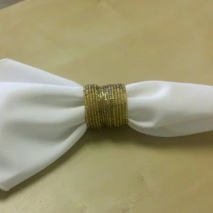 Gold metallic napkin ring wraps around crisp white fabric napkin on neutral background.